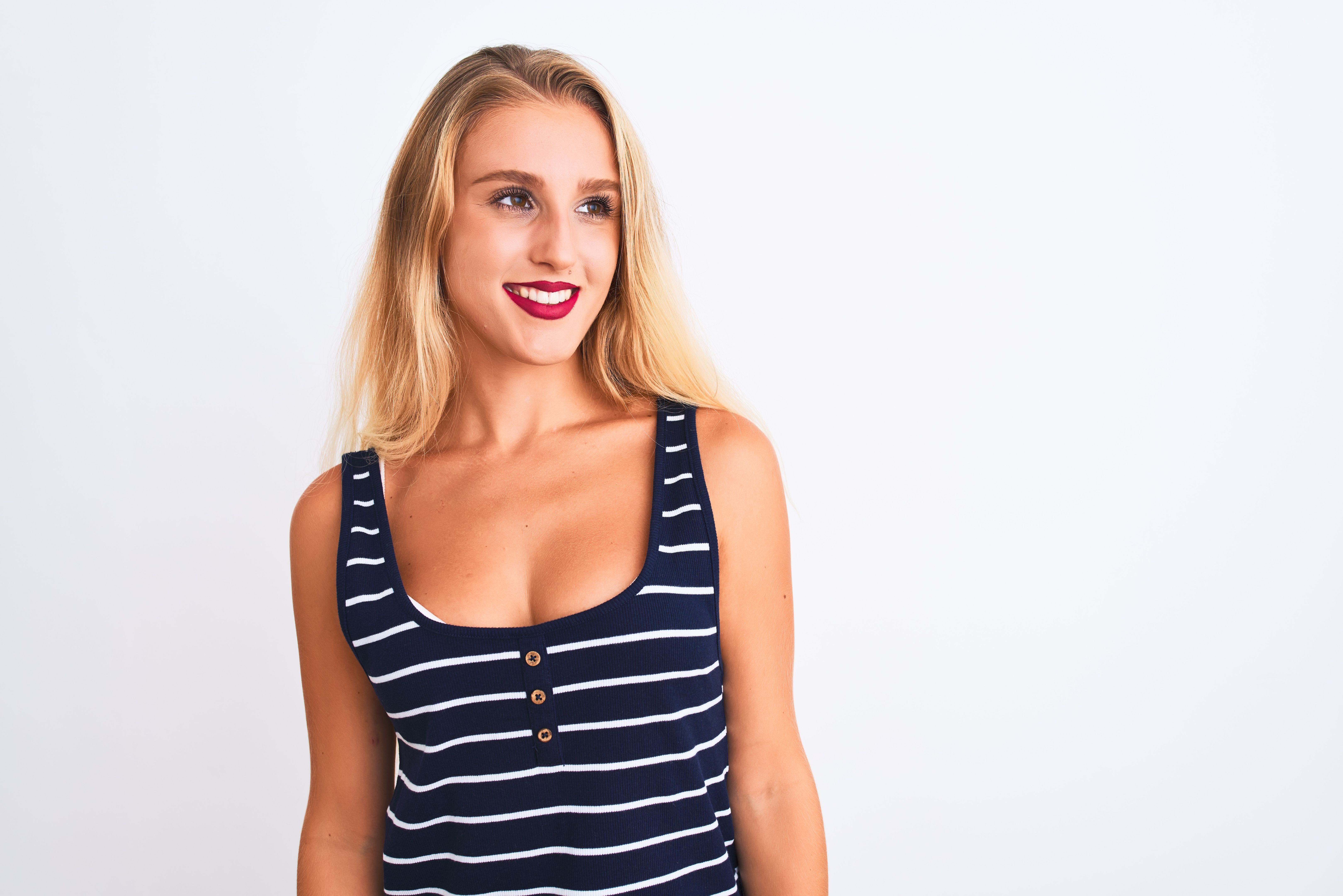 Young beautiful woman wearing casual striped t-shirt standing over isolated white background looking away to side with smile on face, natural expression. Laughing confident.