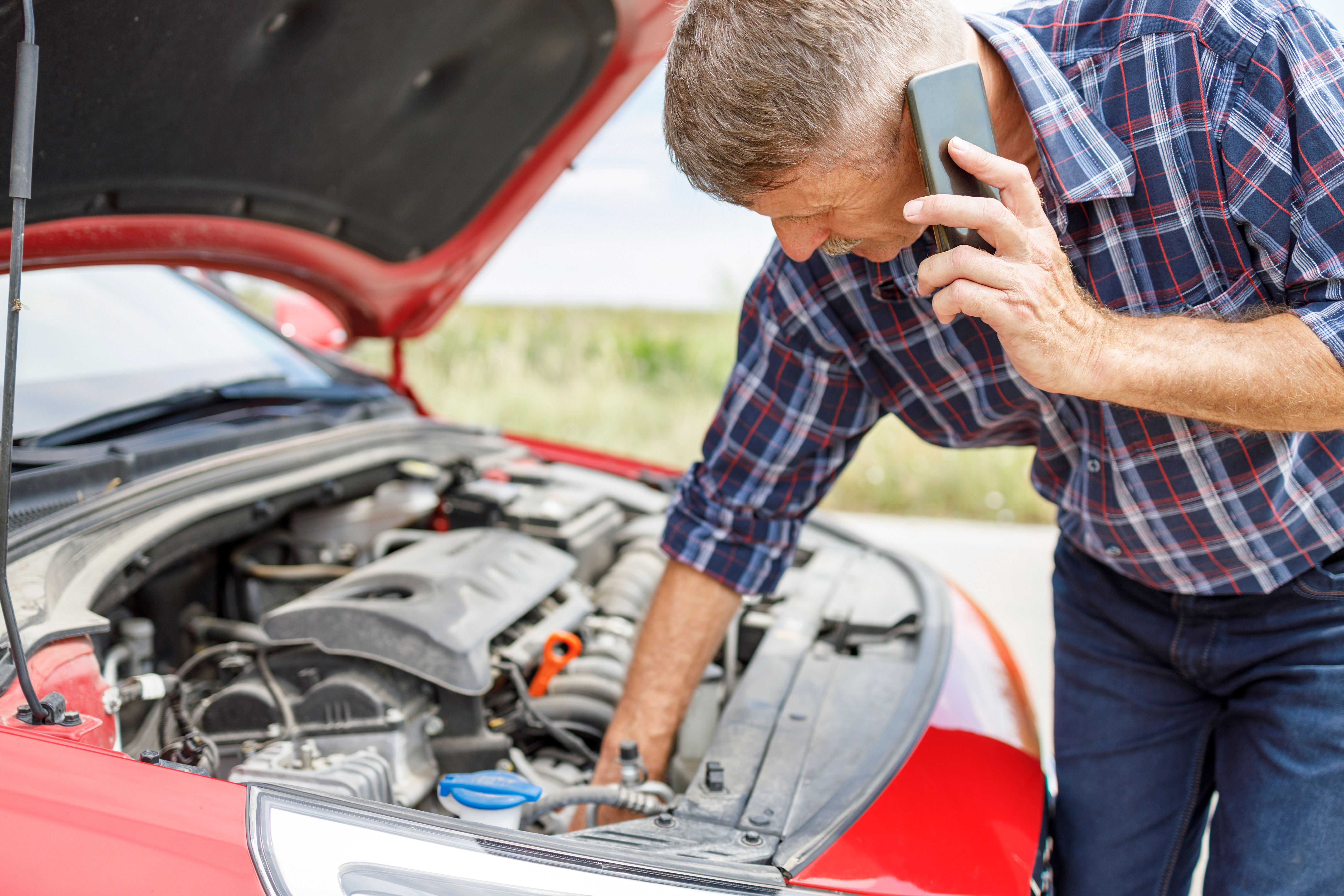 Hombre sosteniendo el teléfono inteligente y recogiendo piezas de la capucha de un coche