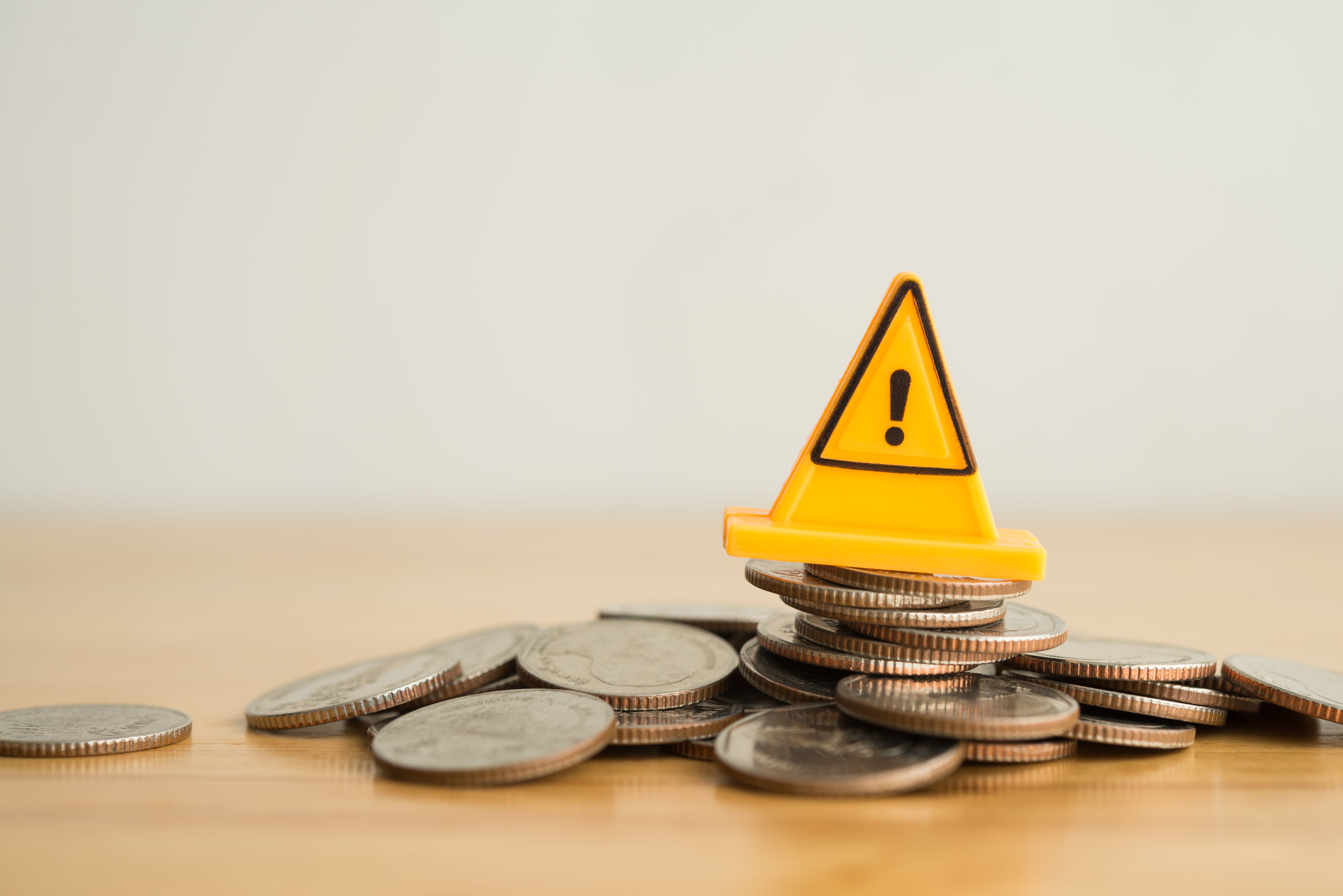 Yellow warning sign label on stack coins crash on wooden table with white background copy space.