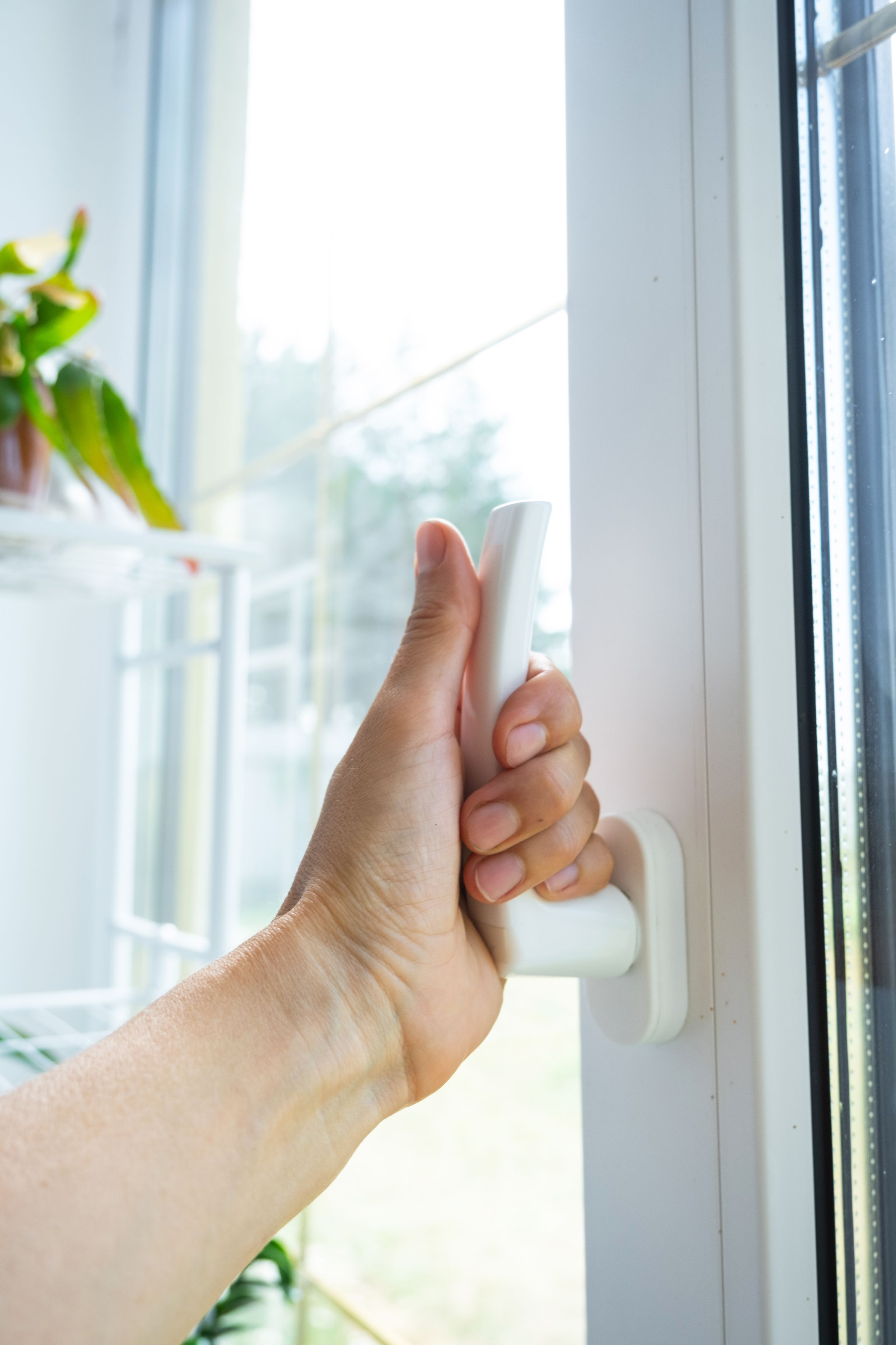 The hand holds the handle of a plastic double-glazed window, closing and opening the window with a rotary mechanism, the position of the handle for ventilation, micro-ventilation