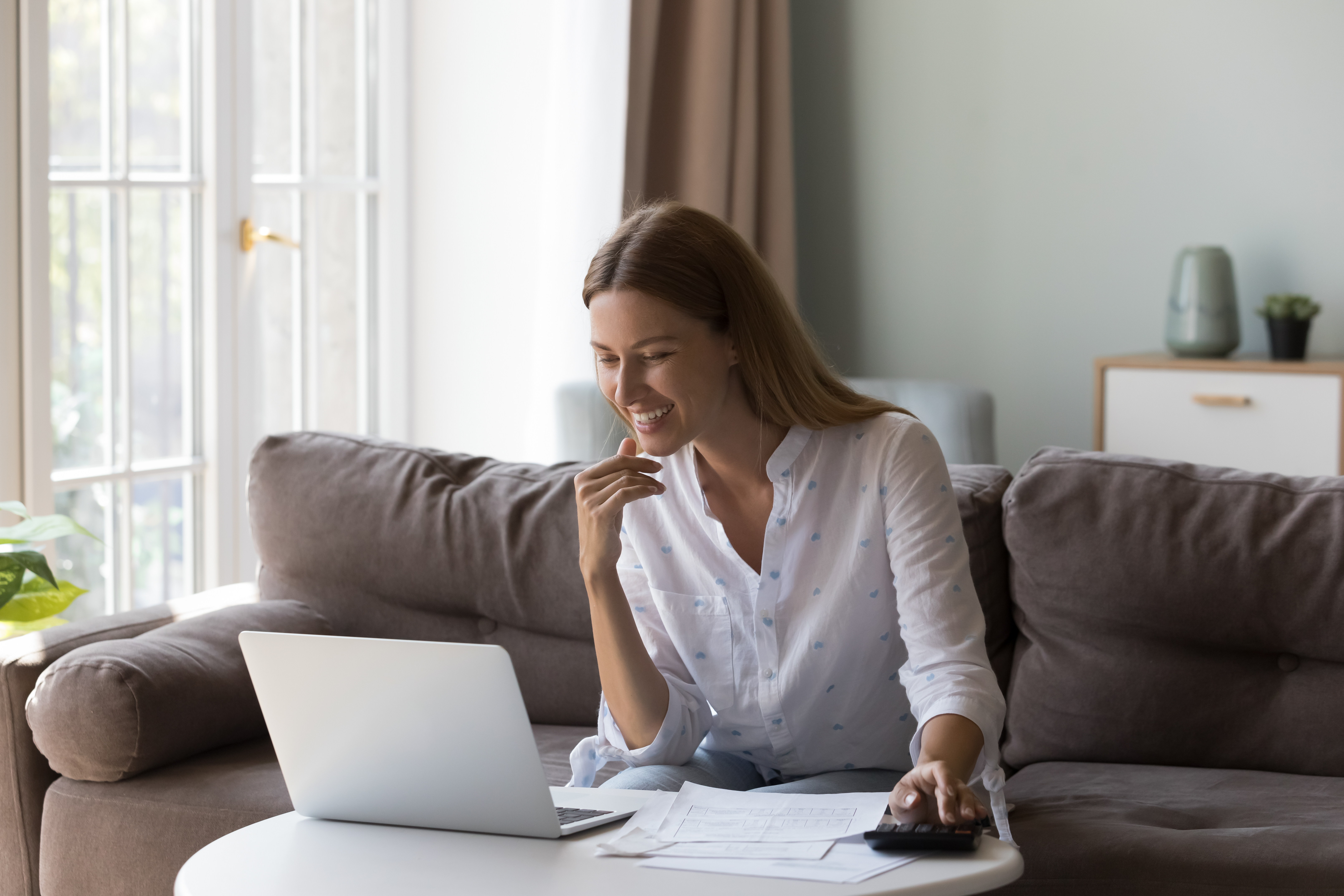 Woman sits at table with laptop counts incomes looks satisfied Woman sits at table with laptop counts incomes looks satisfied