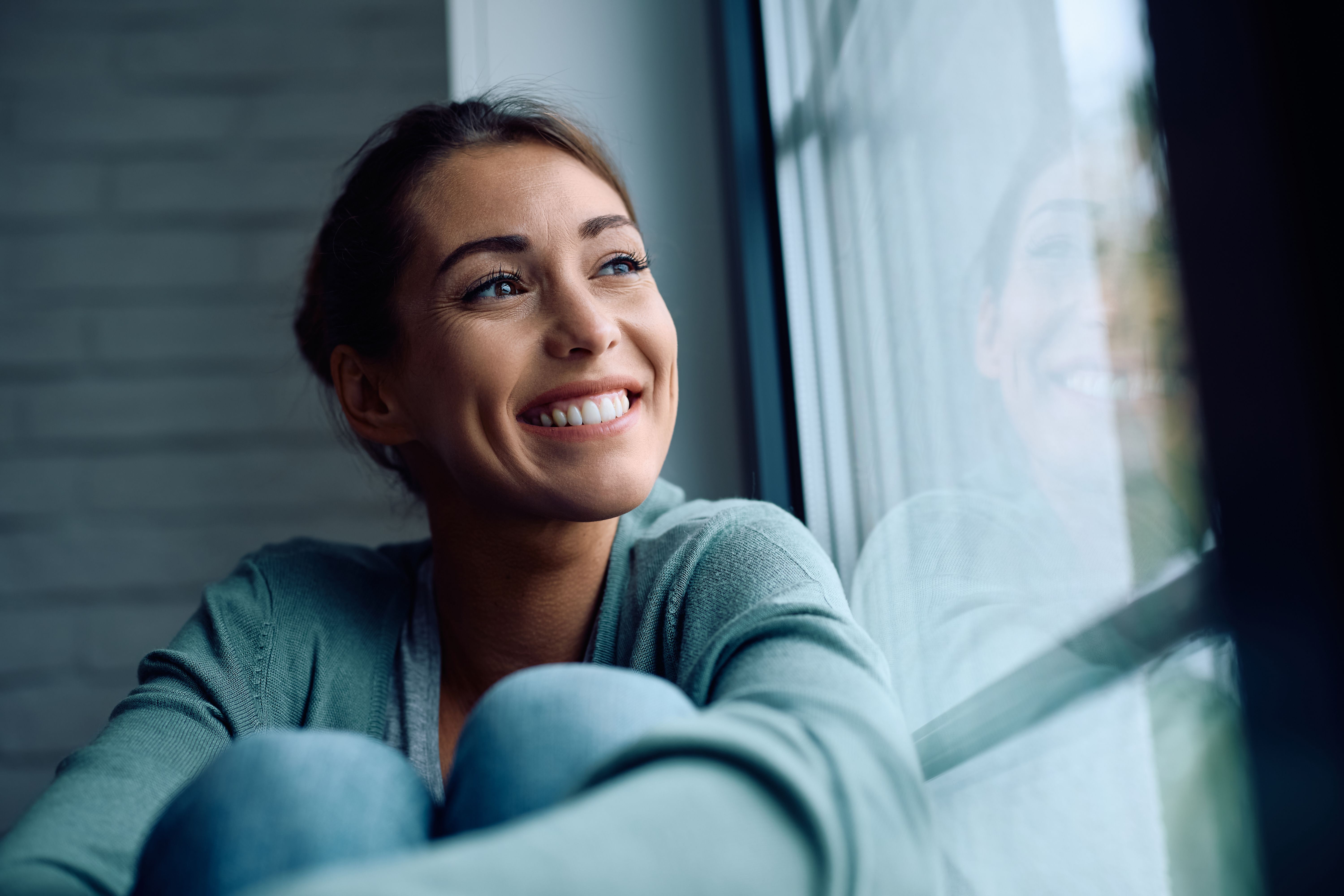 Young happy woman enjoying the view from her home window.