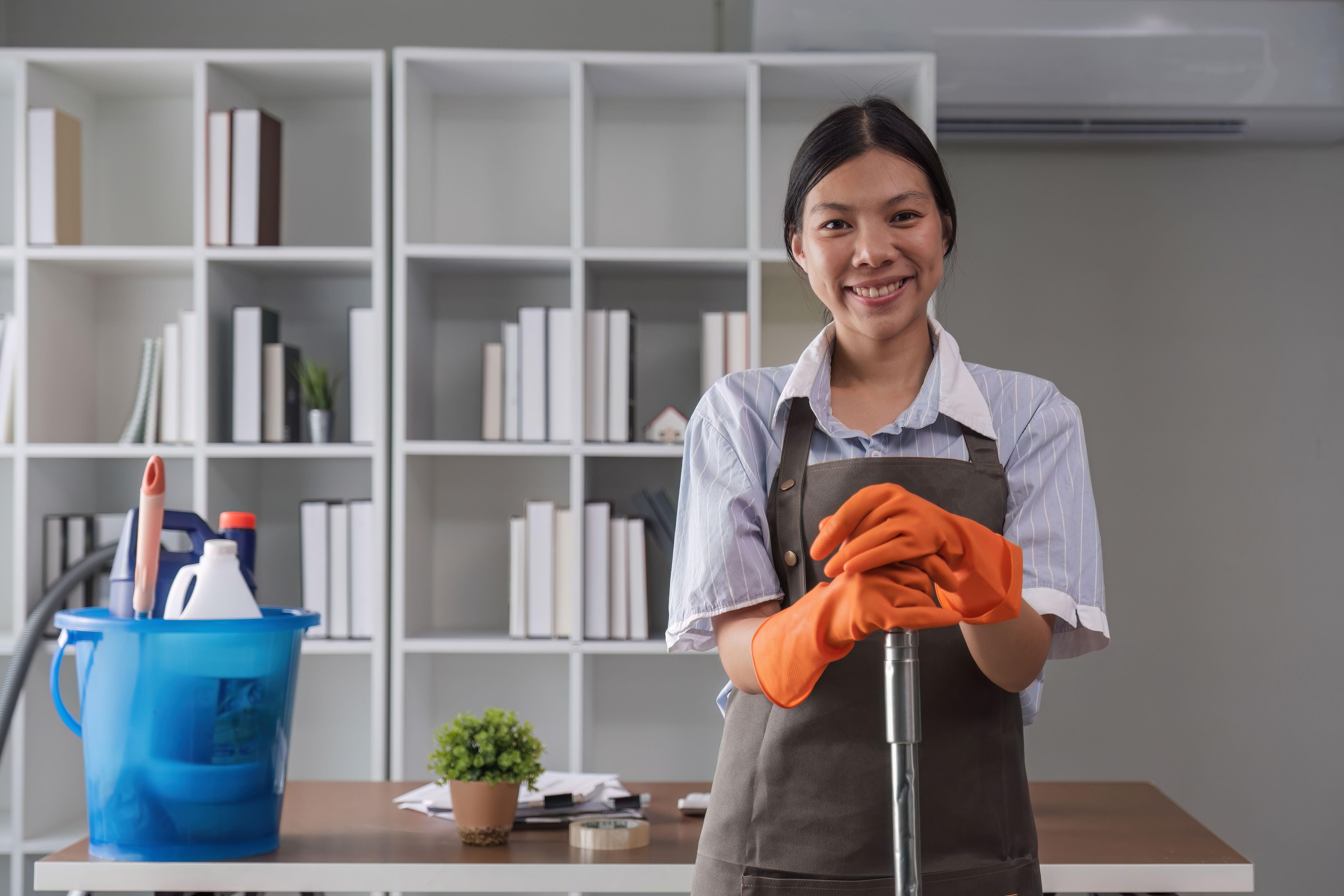 Portrait of a beautiful young housewife smiling and happy, holding cleaning supplies in the office. cleaning supplies, housekeeper