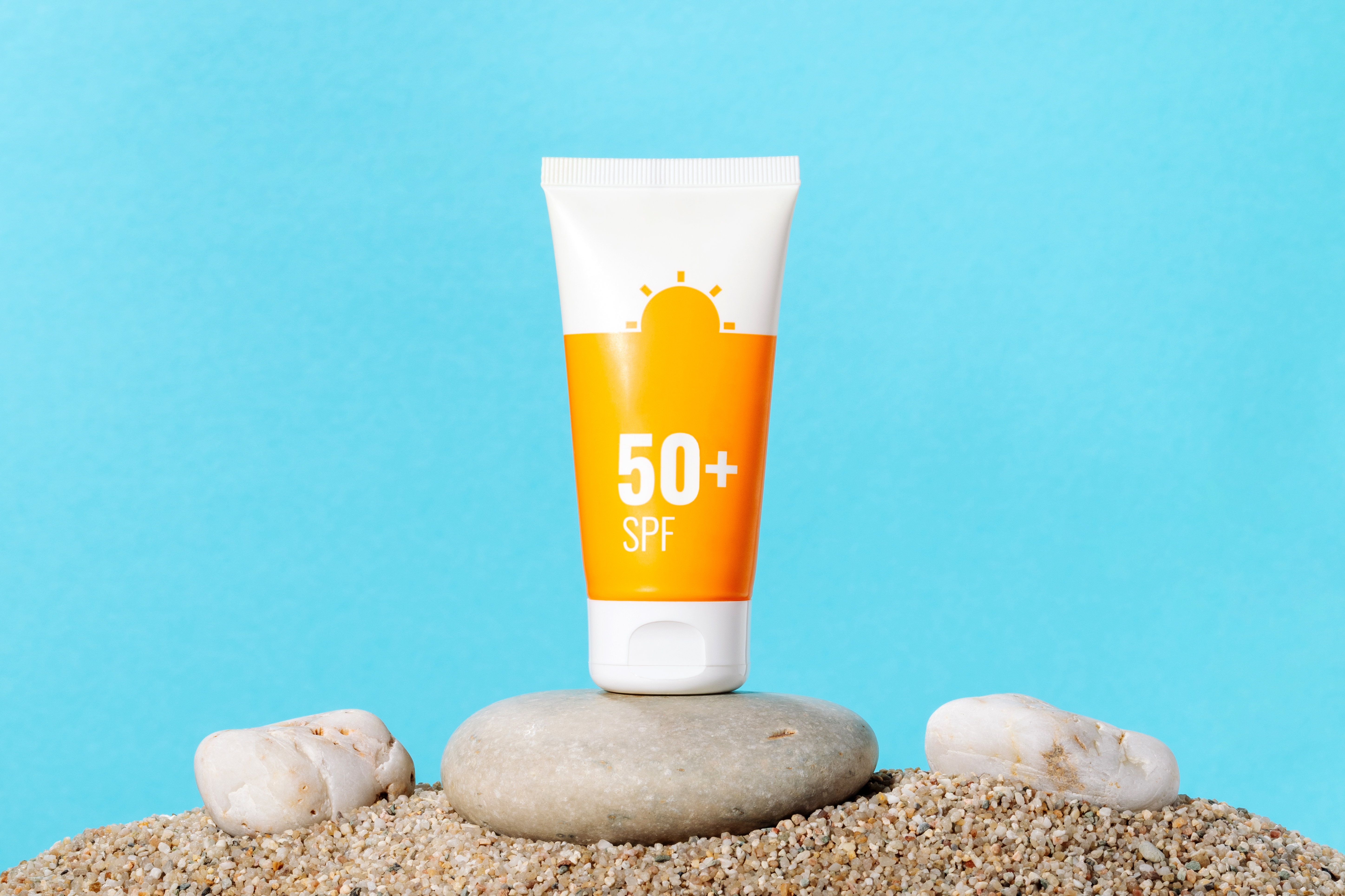 Sunscreen in an orange tube on blue background with beach sand, copy space. Summer beach, vacation concept, spf uv-protect cosmetics Sunscreen in an orange tube on blue background with beach sand, copy space. Summer beach, vacation concept, spf uv-protect cosmetics