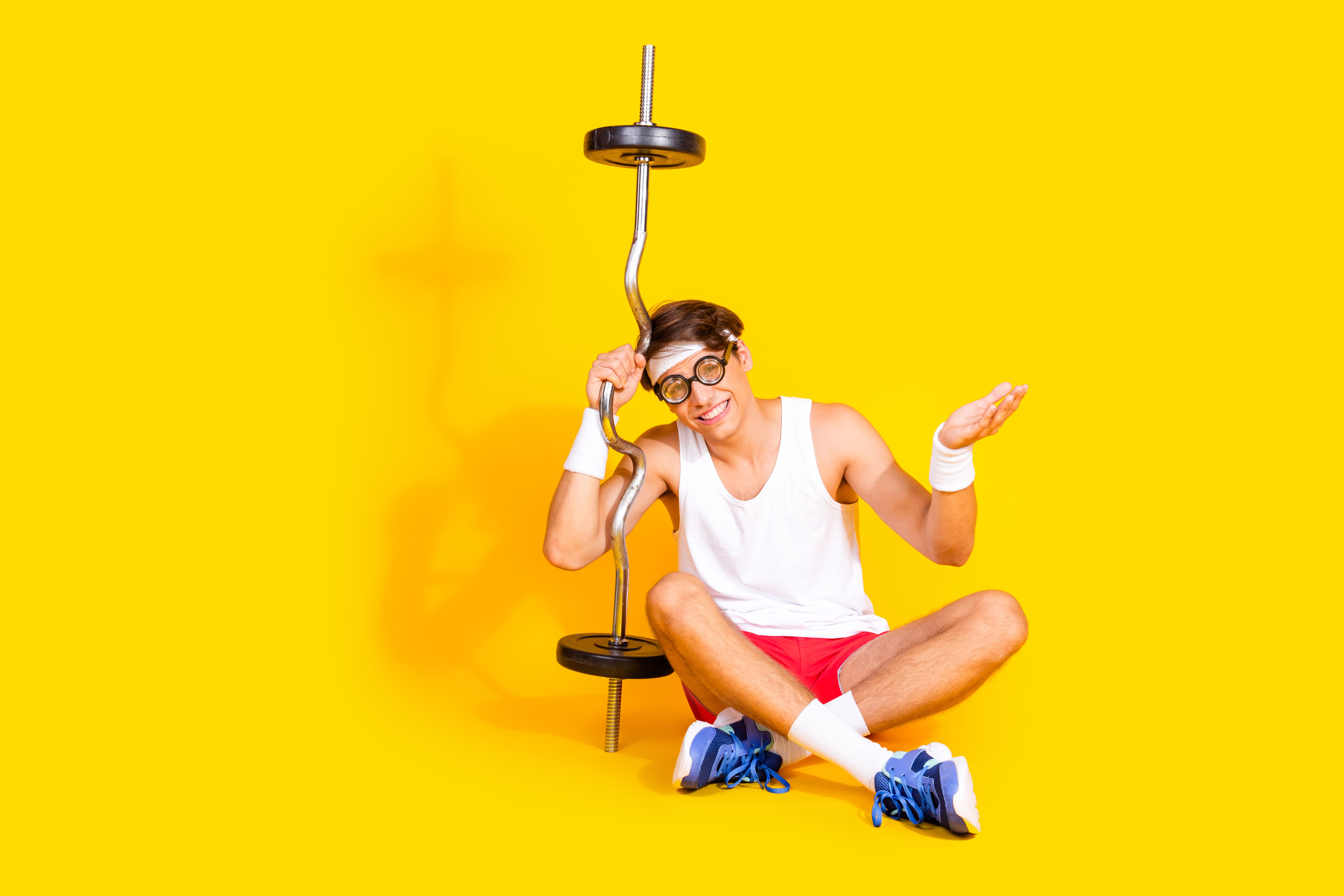 Young man in sportswear sitting with a barbell on vibrant yellow background showcasing healthy lifestyle and fitness Young man in sportswear sitting with a barbell on vibrant yellow background showcasing healthy lifestyle and fitness
