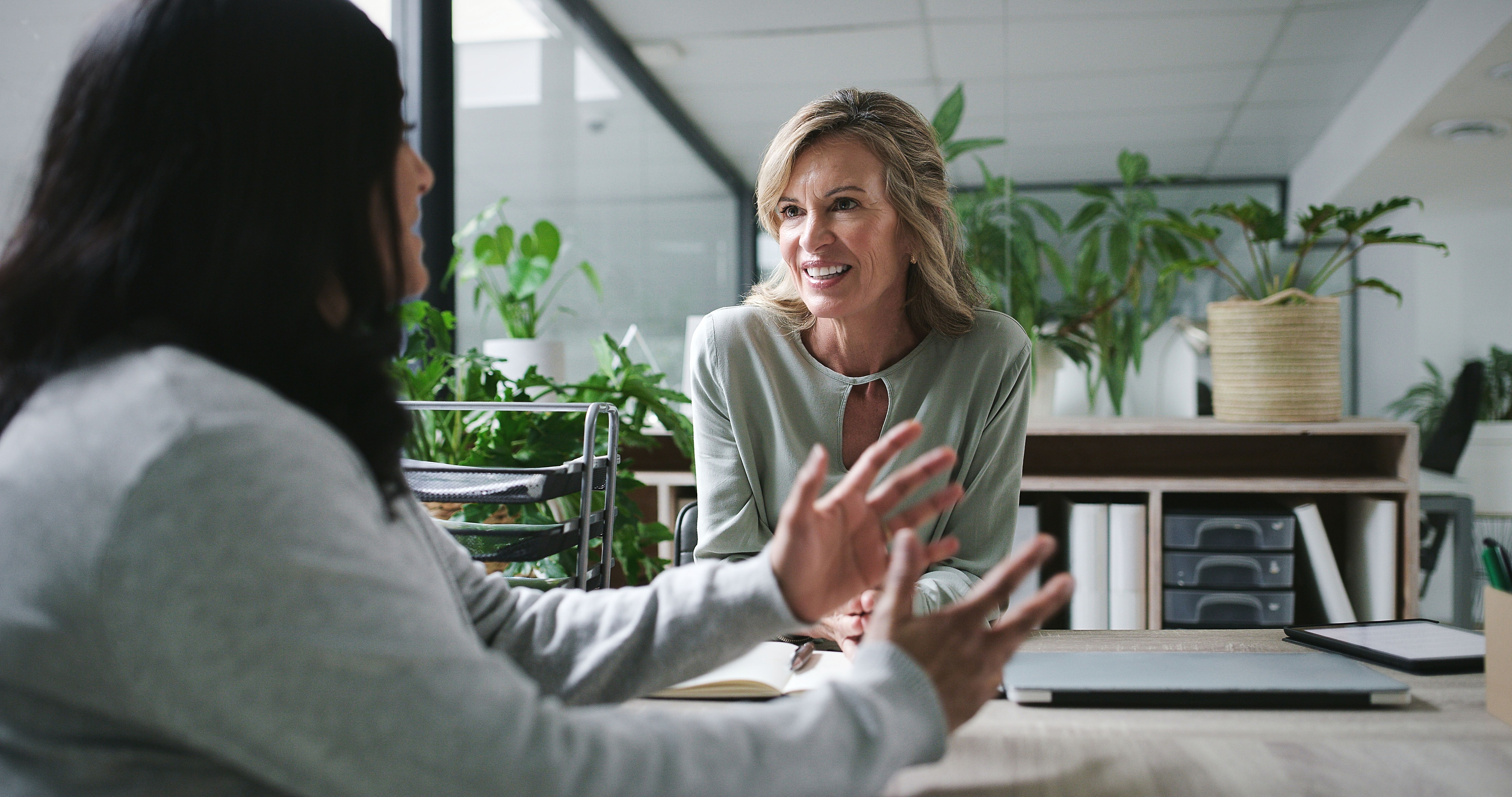 Meeting, conversation and business women in office for project performance review in career. Happy, talking and female manager with creative designer for discussion by desk in startup workplace.