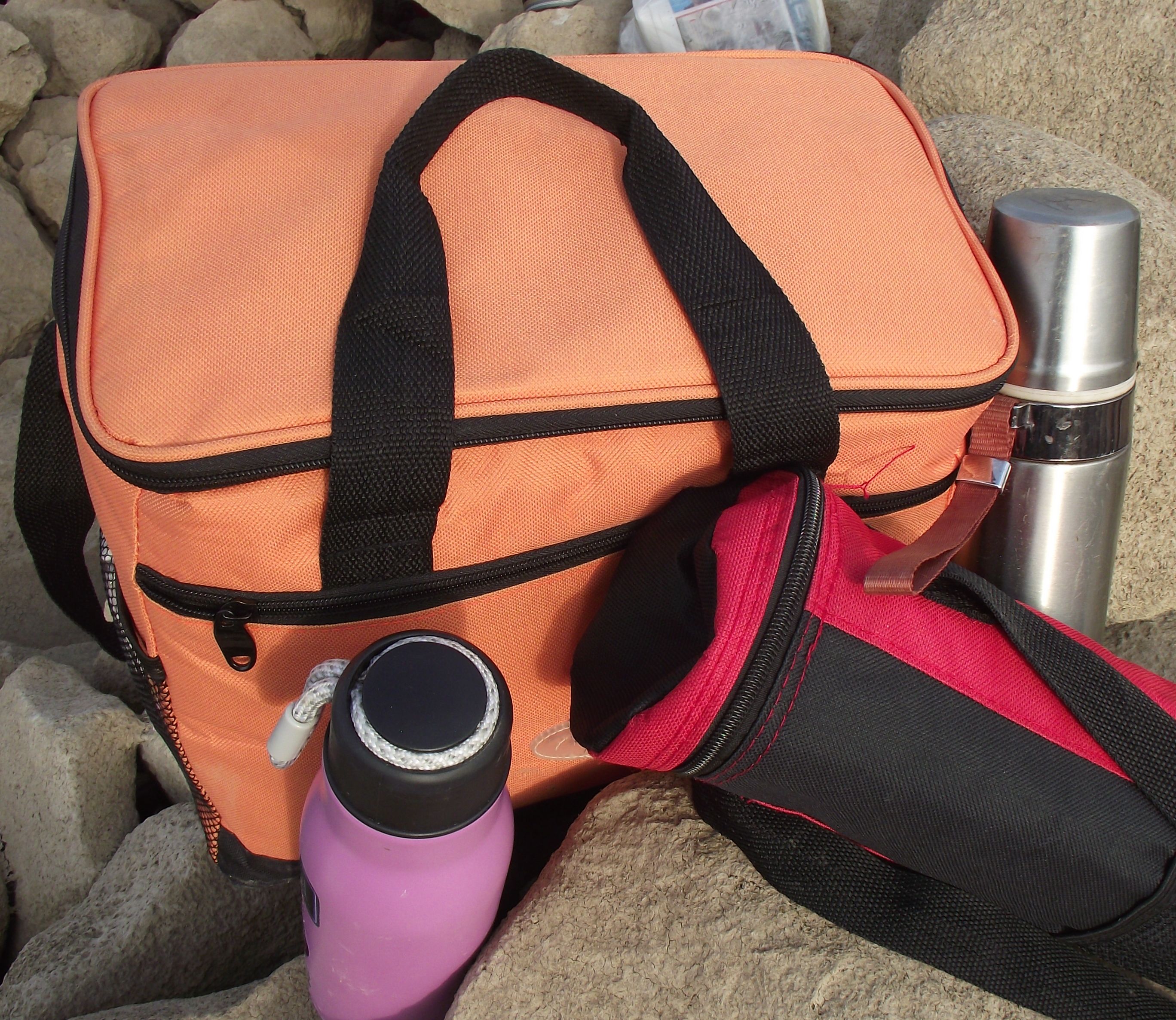 bottles of thermoses and a refrigerator bag lie on the stones at the parking lot of tourists