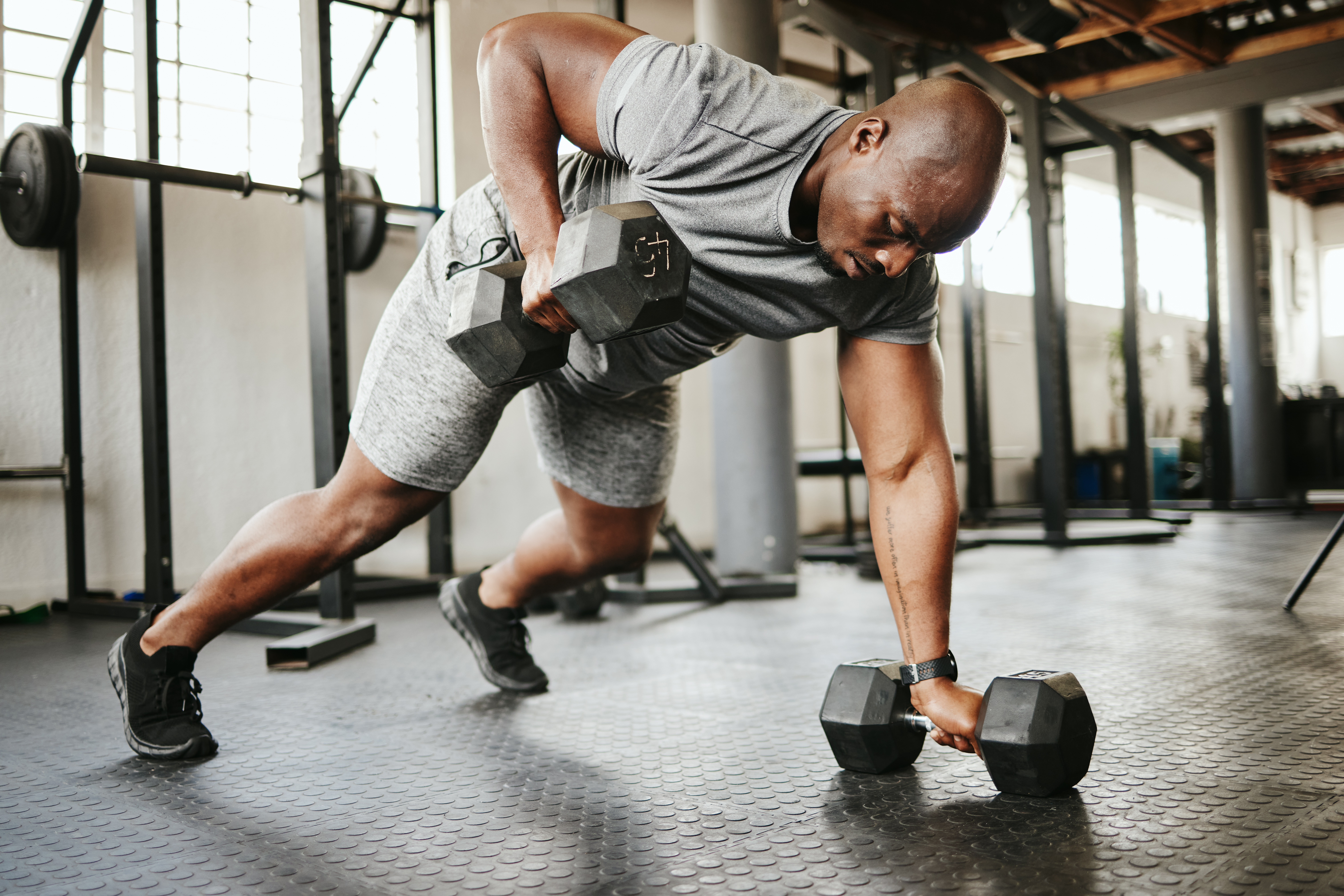 Dumbbell, fitness and bodybuilder black man with workout training in gym or garage studio for wellness, body goal and motivation. Power, strong and african sports man doing push up exercise with gear