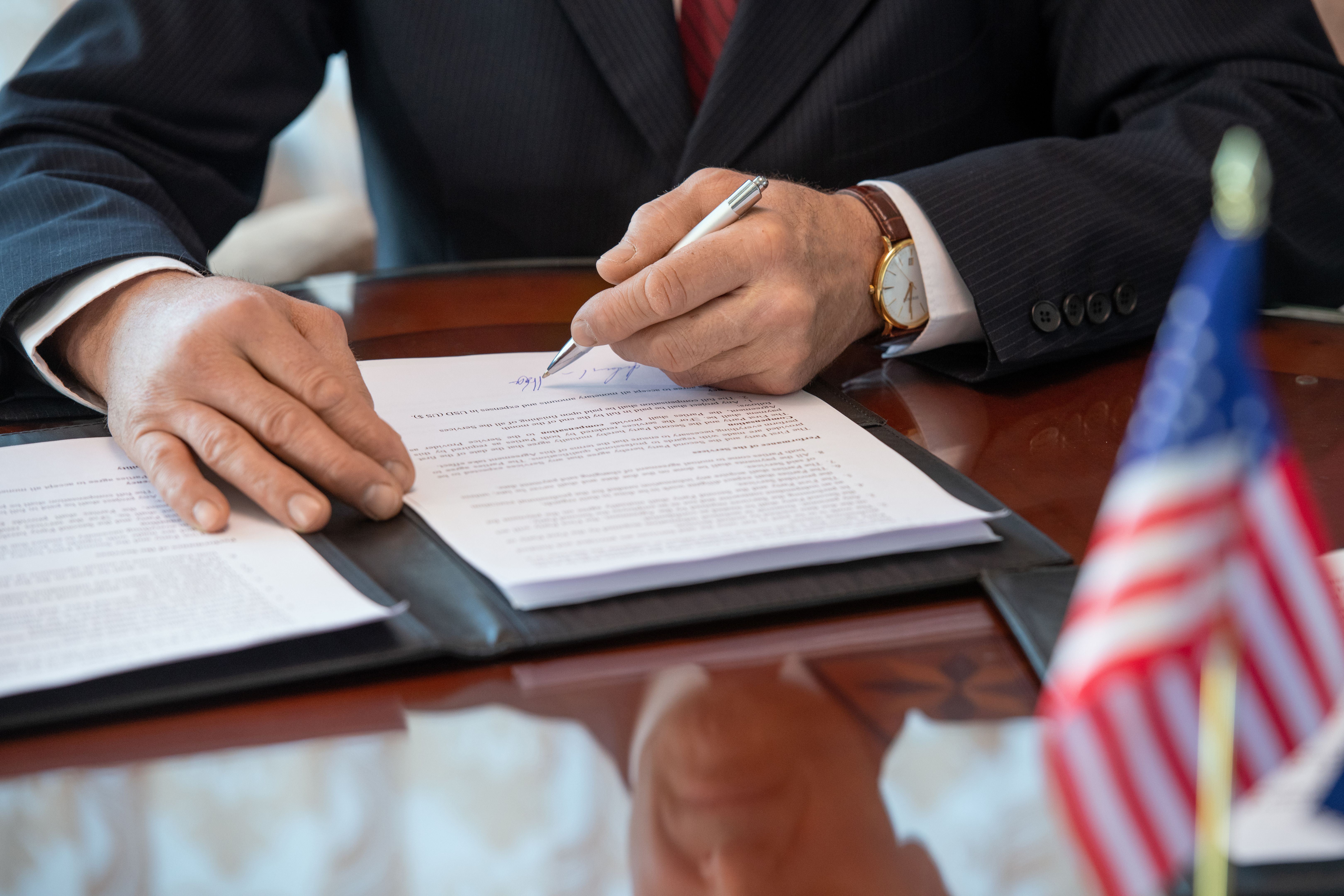 Hands of mature American delegate in formalwear pointing at signature in contract