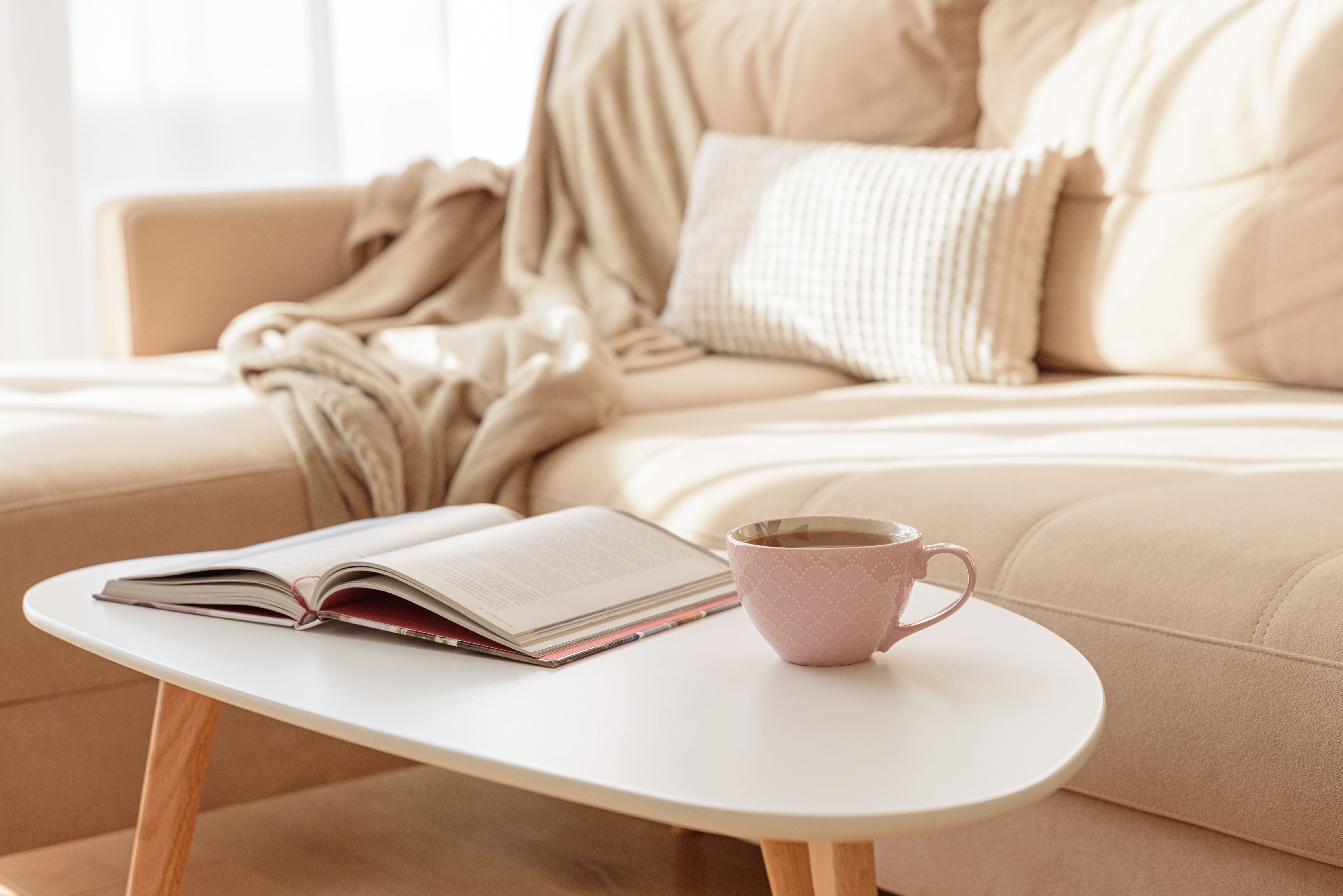 Cozy living room with a book and tea on a beige couch. Soft focus