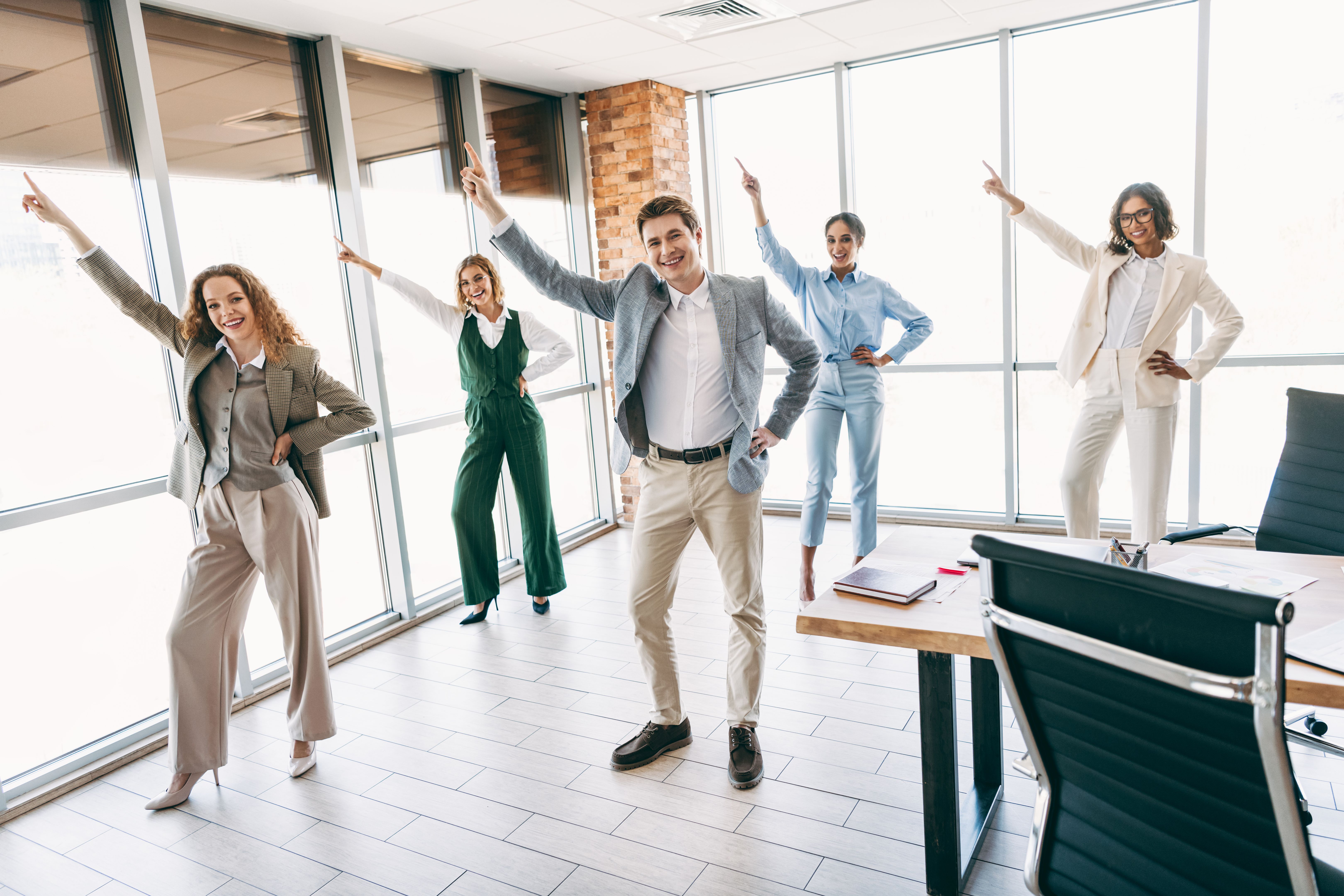 Group of professional colleagues in office attire collaborating energetically, standing in unison, displaying teamwork