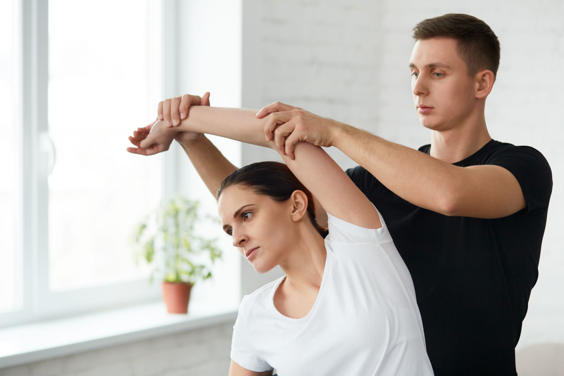 Female patient doing physical exercises with physiotherapist. Male therapist treating injured shoulder of young athlete. Post traumatic rehabilitation, sport physical therapy, recovery concept.