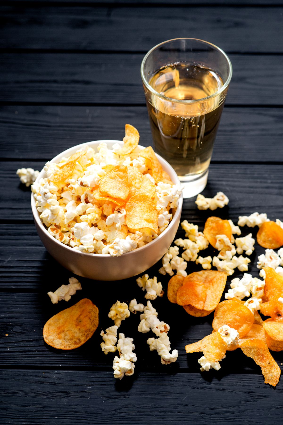 cheese popcorn in the bowl with a glass of beer and potato chips on the wooden background
