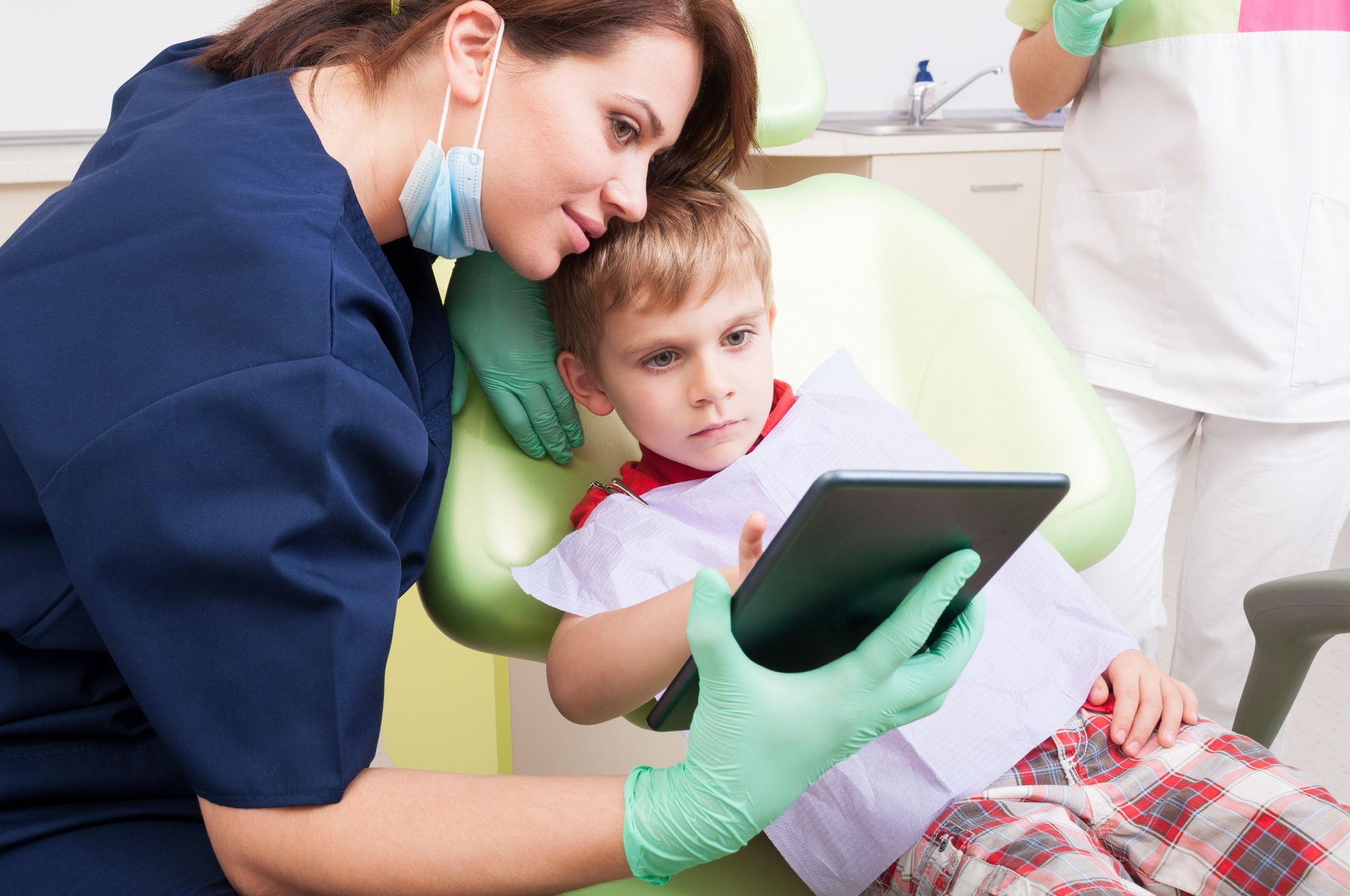 Modern dentist use wireless tablet with kid patient. Child having fun and playing in dentist chair