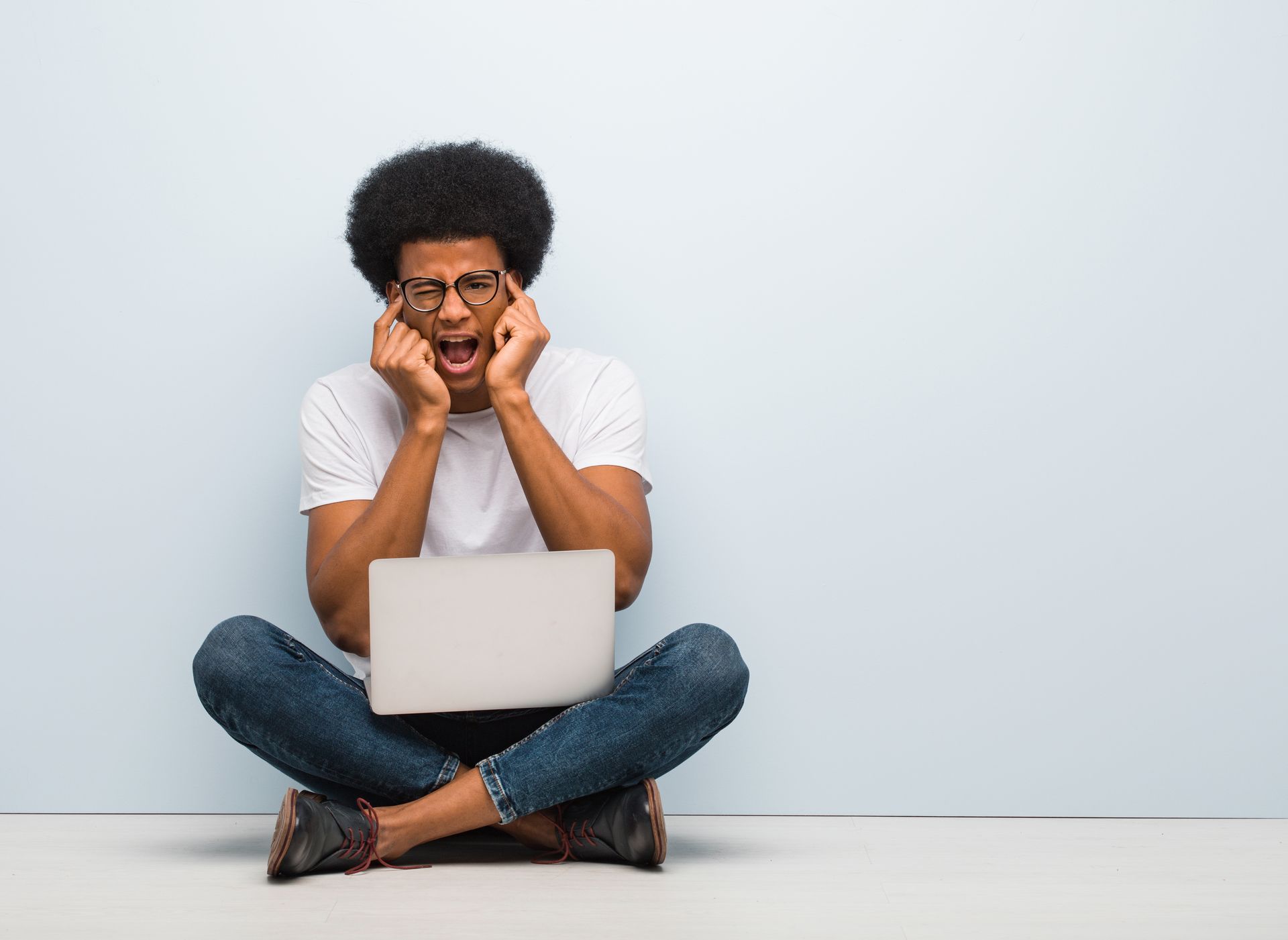 Young black man sitting on the floor with a laptop desperate and sad