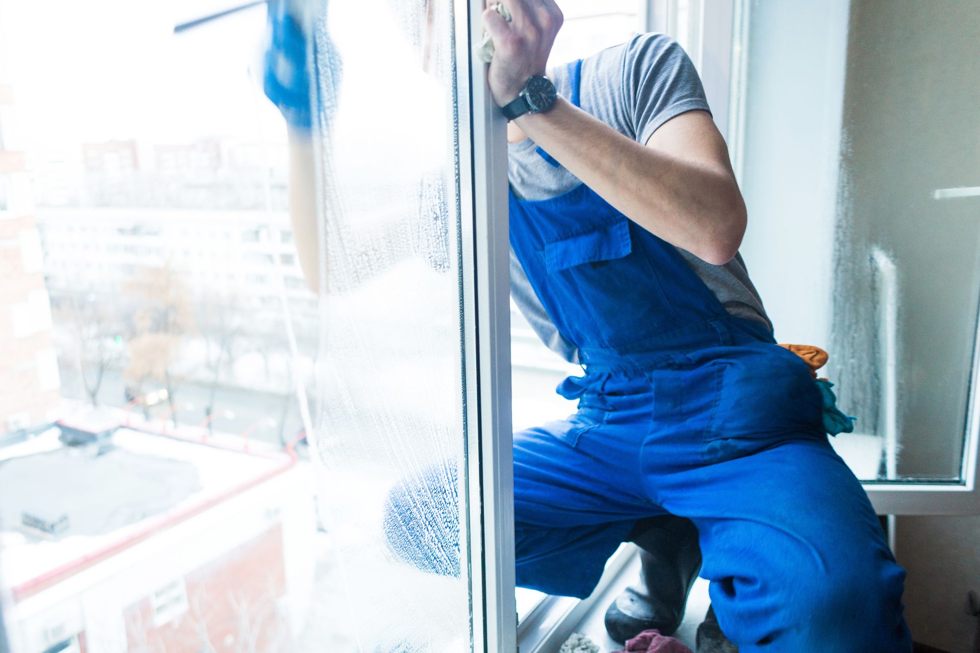 Close-up of a man in uniform and blue gloves washes a windows with window scraper. Professional home cleaning service