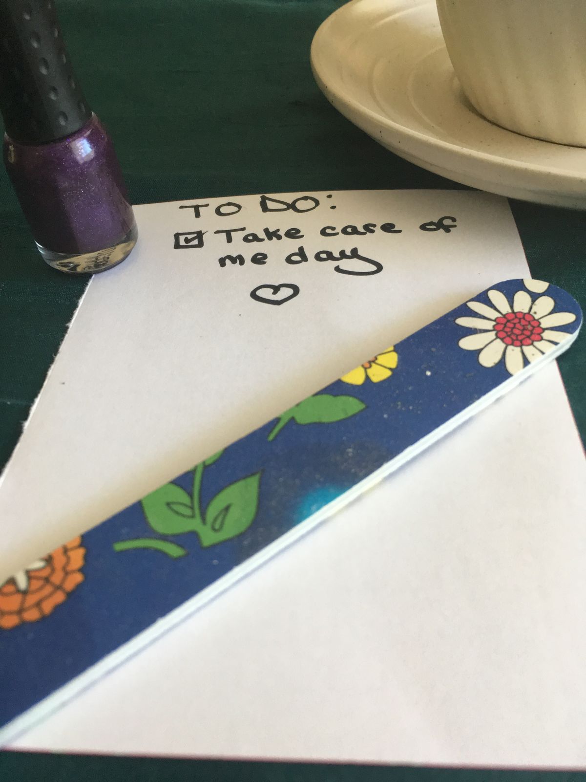 Nail polish, nail file, a tea cup, and a self-care reminder