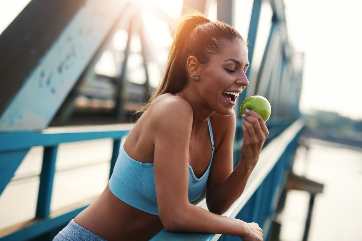 Fit and sporty young woman having break from running and eating apple