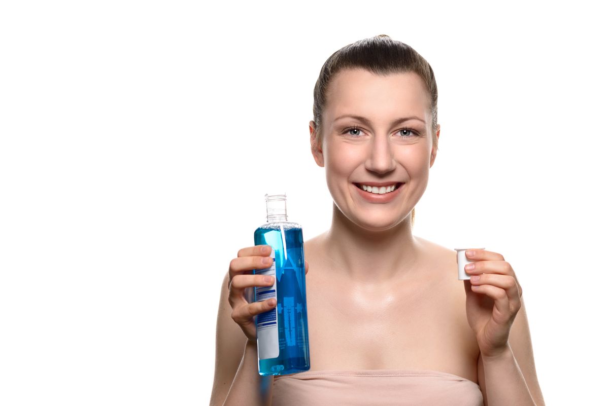 Close up Smiling Young Woman holding a Bottle of Mouthwash into a Cap While Looking at the Camera, Isolated on White Background.