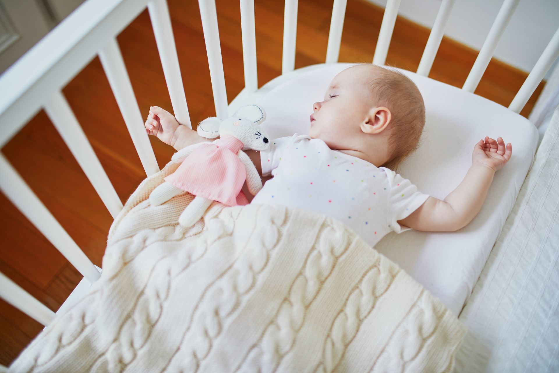 Adorable baby girl sleeping in co-sleeper crib attached to parents' bed with stuffed toy. Little child having a day nap in cot. Sleep training concept. Infant kid in sunny nursery
