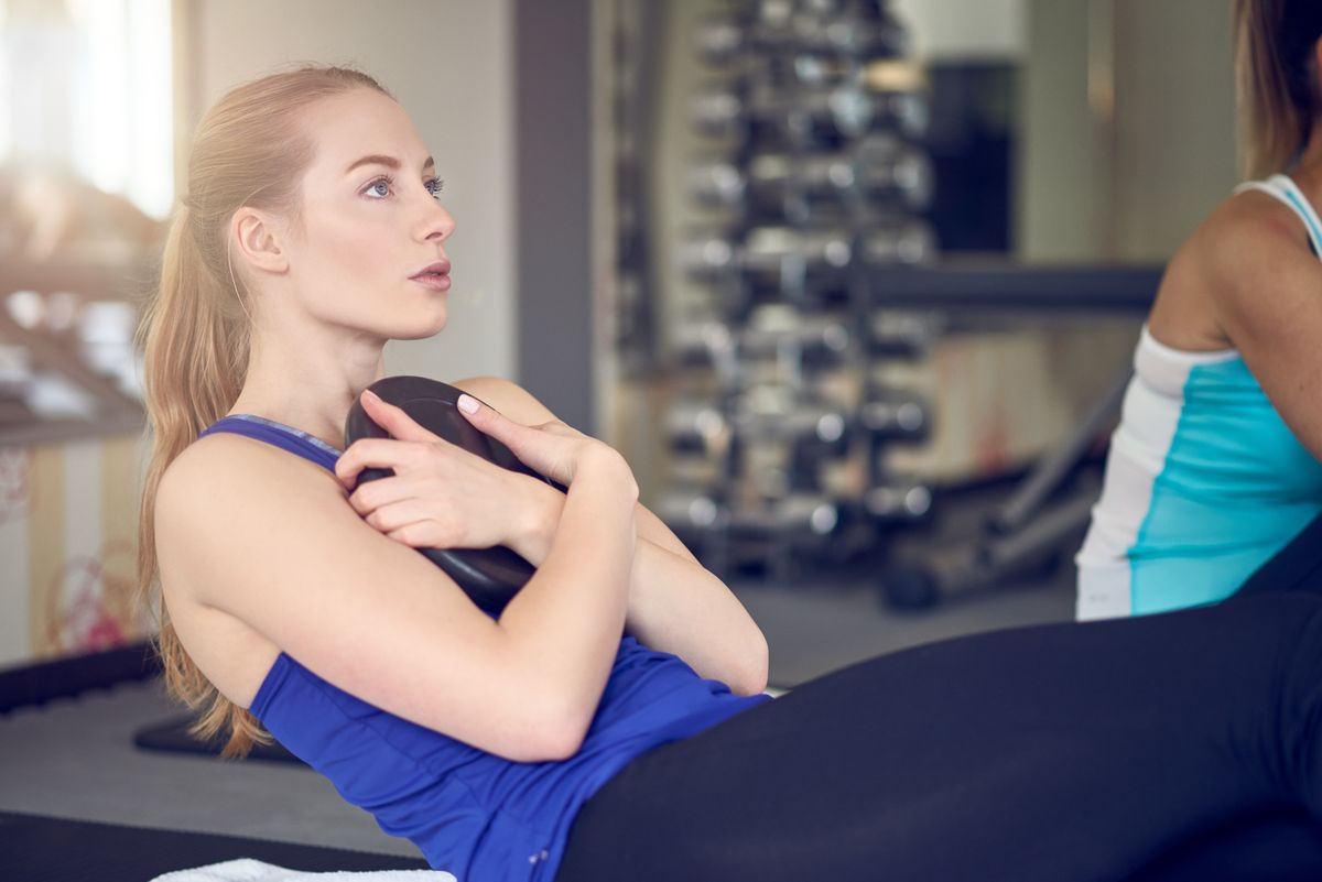 Pair of young adult women doing abdominal muscle Russian twist exercises while holding weights