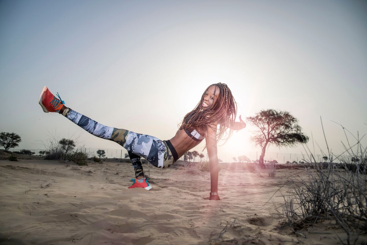 Strong African Black woman with long braids in har in the desert in sportswear does a body weight exercise with a dramatic sunrise or sunset in the background  