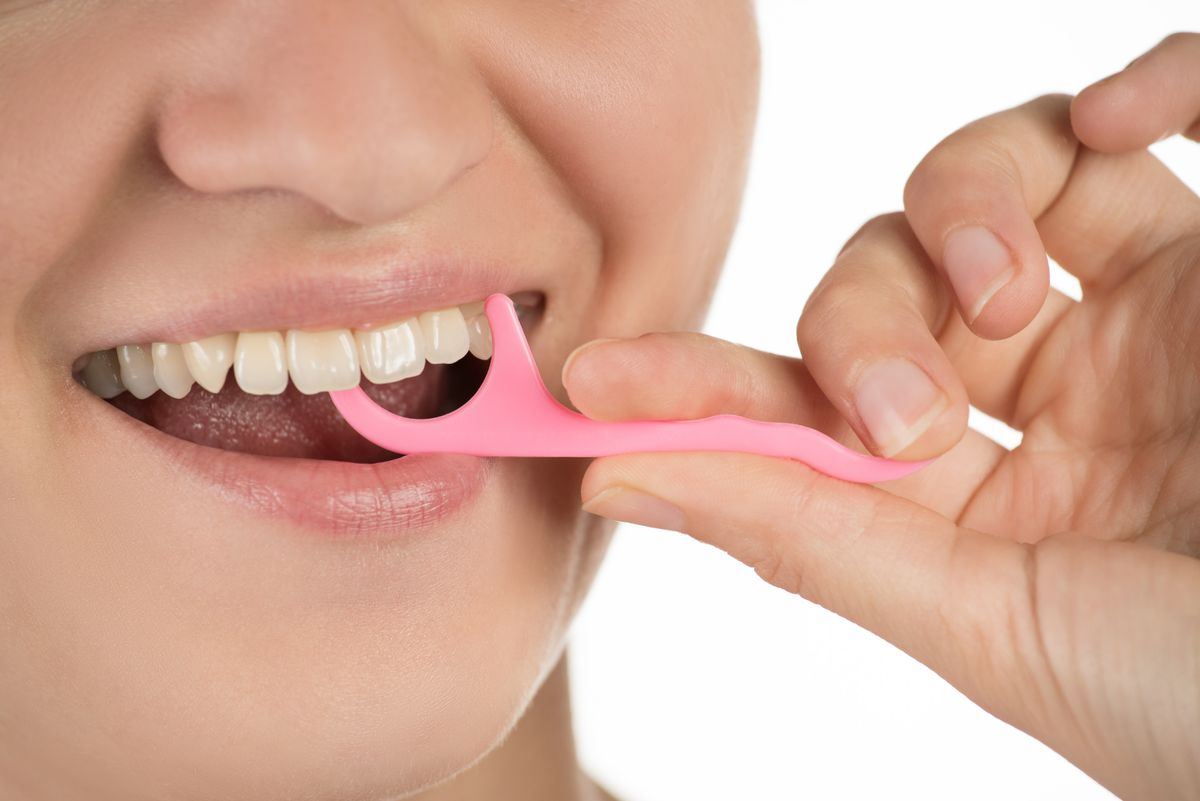Hygiene of the oral cavity. Young girl cleans teeth with floss, smiling and showing okay sign on white background.