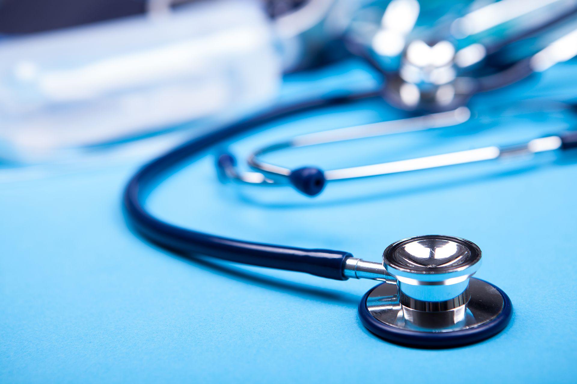 Close up photo of stethoscope lying in front of other blurred medicinal equipment on blue background