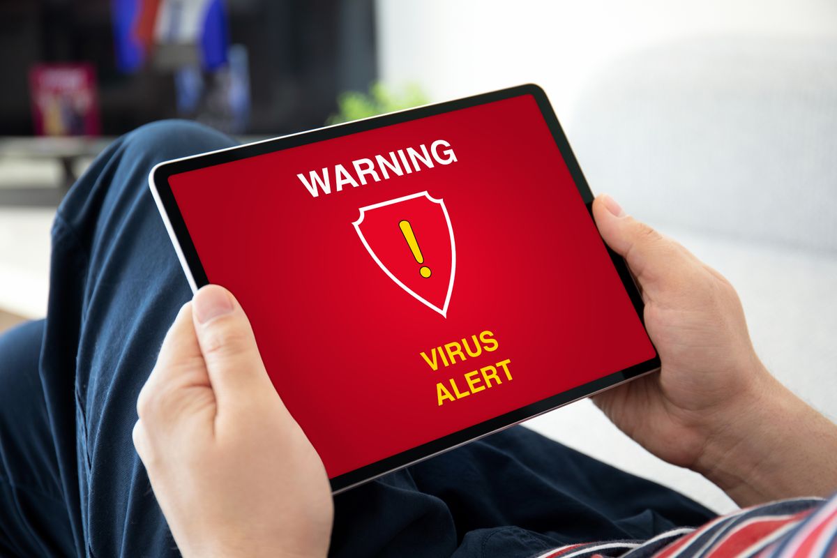 man hands holding computer tablet with warning virus alert on the screen in the house room