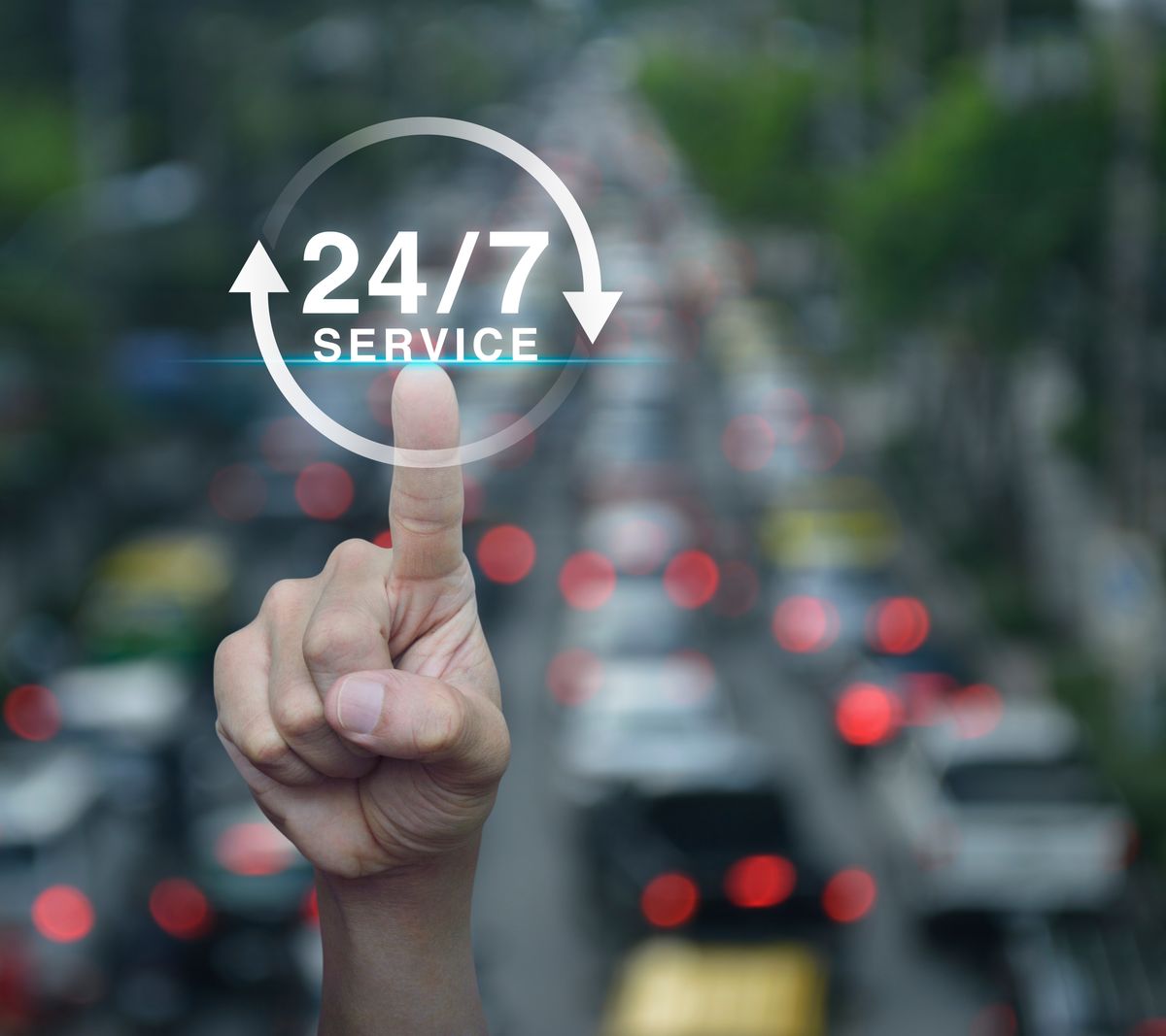 Hand pressing button 24 hours service icon over blur of rush hour with cars and road, Full time service concept